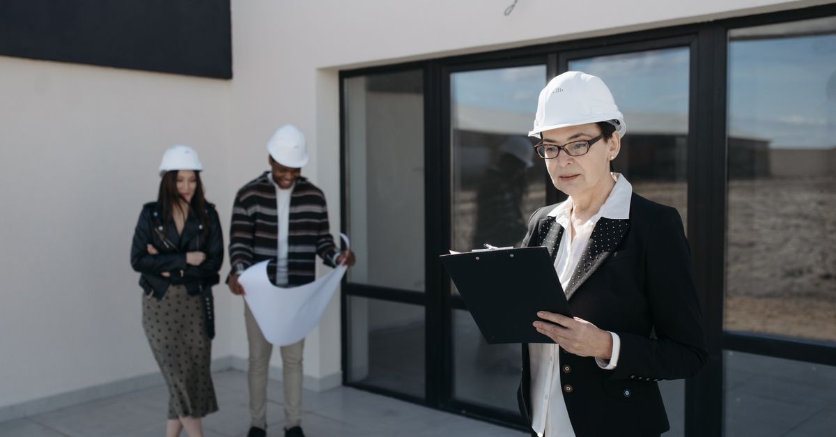 Architects in hard hats examining construction plans at a building site.